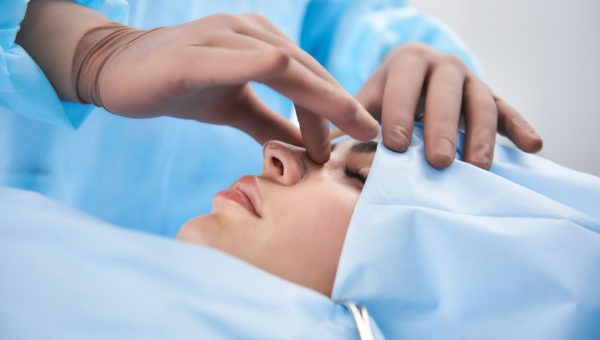 Surgeon in rubber gloves making rhinoplasty for woman