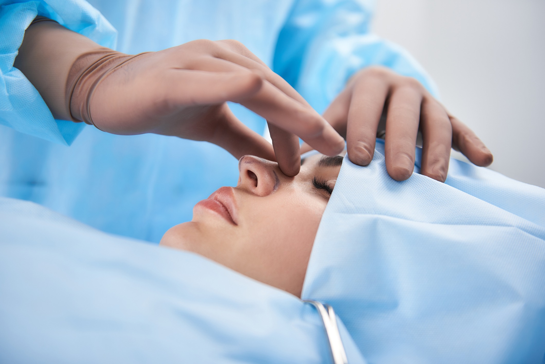 Surgeon in rubber gloves making rhinoplasty for woman